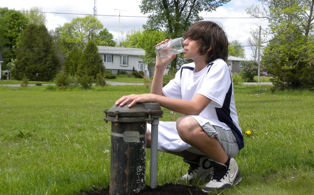 Teen beside a drilled well drinking a glass of water