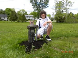 Teen kneeling beside a drilled well with a tall glass of water