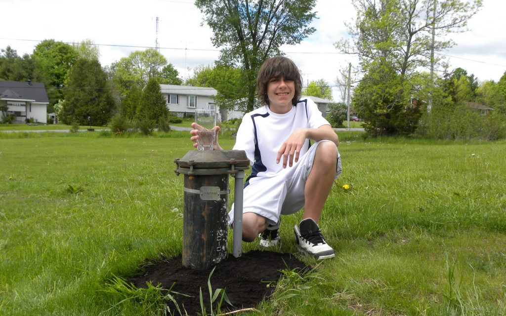 Teen kneeling beside a drilled well with a tall glass of water